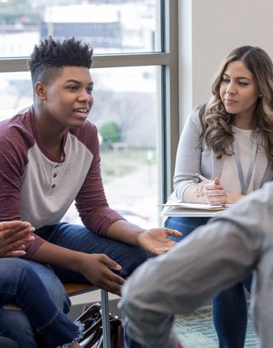 A young man in a counseling session talking to others in the group. A woman next to him is watching and listening to him speak.