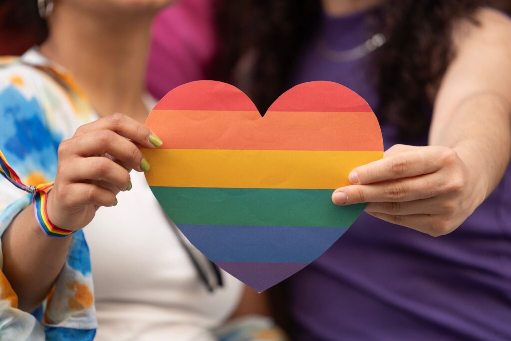 Two individuals holding up a Pride month heart.