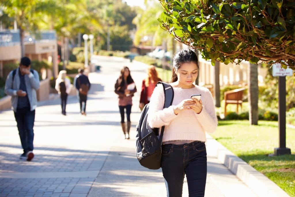 Young adult walking to class while on her phone.