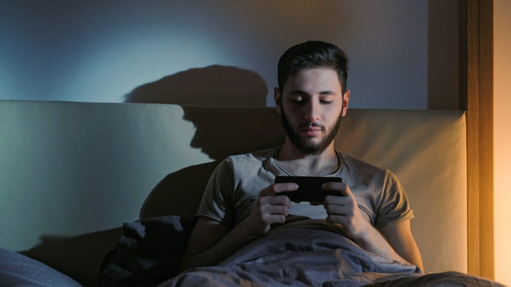 Young adult man on his phone at night in bed.