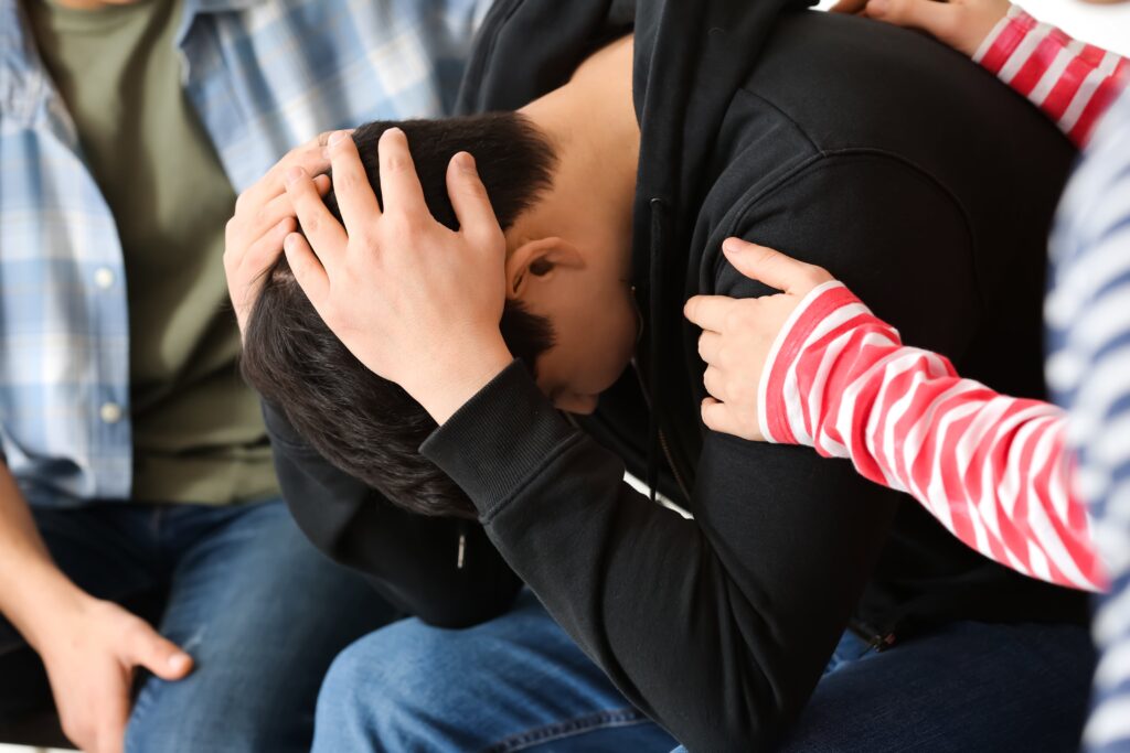 Young adult man being comforted by loved ones.