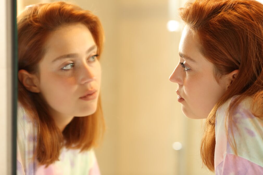 Young adult looking in the mirror at their reflection.