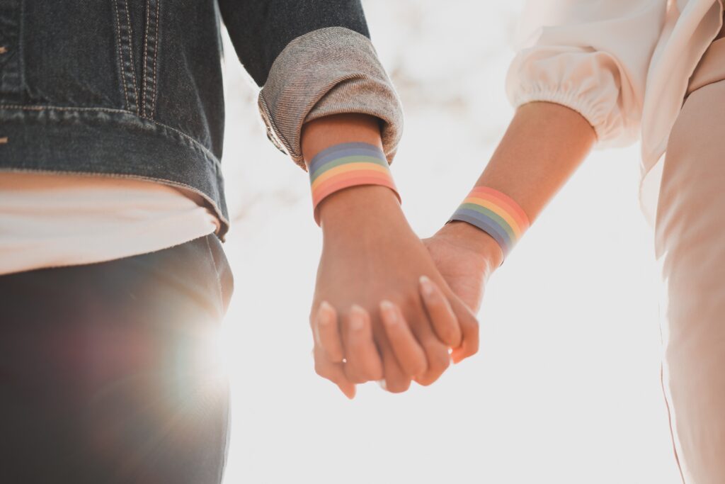 Two people holding hands with LGBTQ+ bands on their wrists.