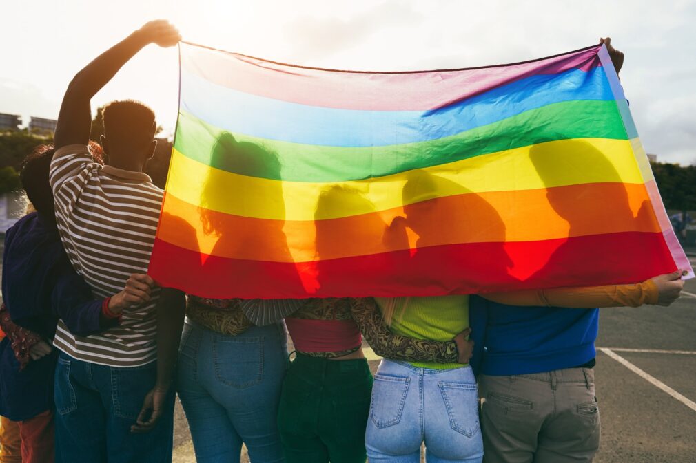 Group of LGBTQ individuals holding up a Pride flag.