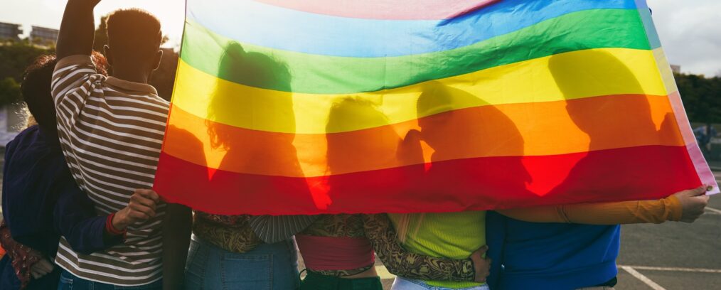 Group of LGBTQ individuals holding up a Pride flag.