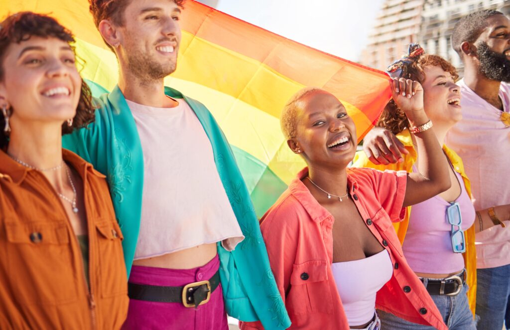 Group of LGBTQ individuals walking together with a Pride flag.