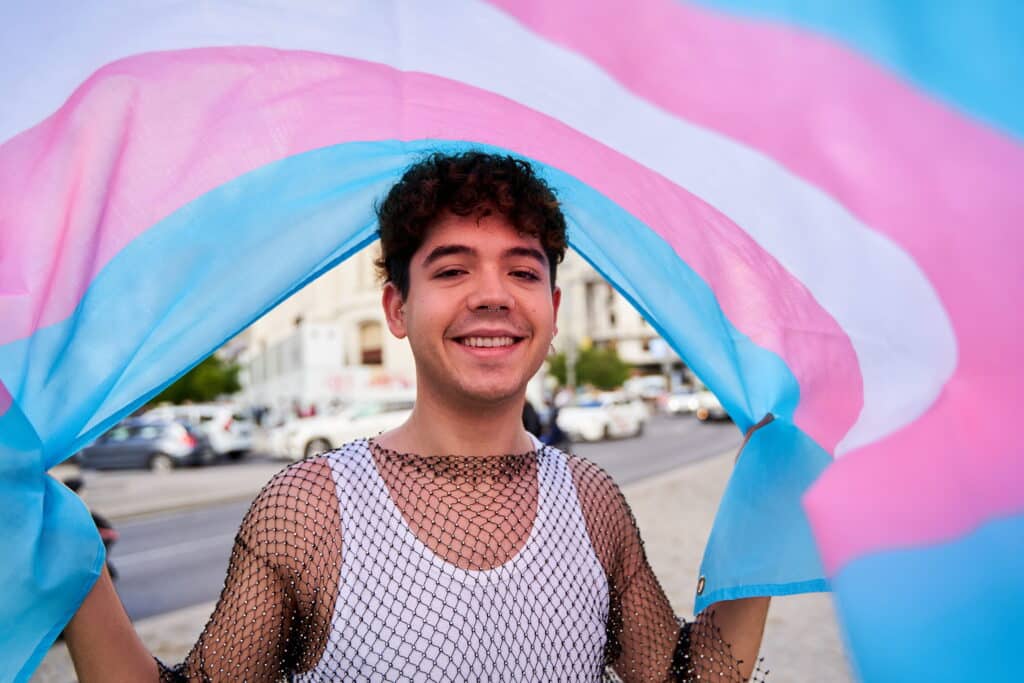 Individual smiling and holding up a transgender flag.