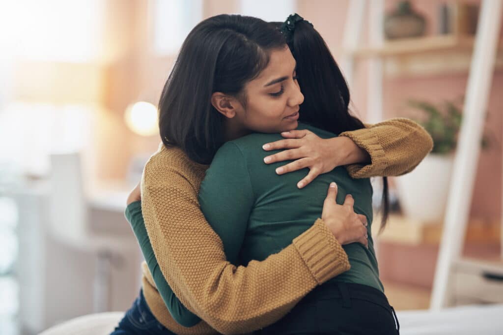 Young adult hugging and comforting her friend.